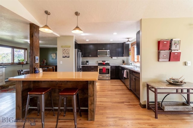 3950 Floweree, Helena, MT 59602 - kitchen featuring appliances with stainless steel finishes, light wood-type flooring, a breakfast bar, decorative light fixtures, and wood counters