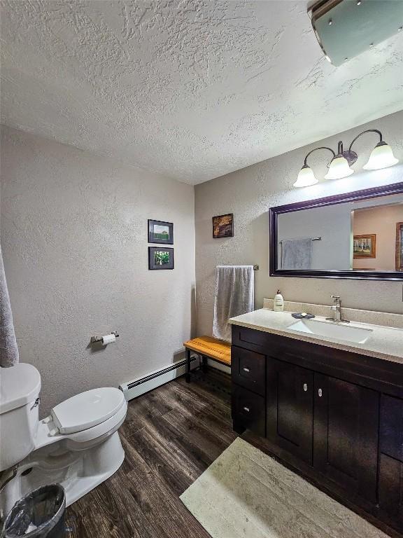 3950 Floweree, Helena, MT 59602 - half bath with a baseboard heating unit, a textured wall, wood finished floors, vanity, and a textured ceiling