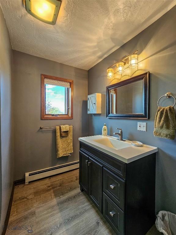 3950 Floweree, Helena, MT 59602 - bathroom featuring baseboard heating, vanity, wood finished floors, and a textured ceiling