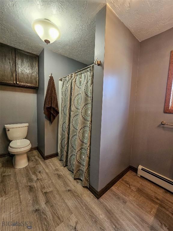 3950 Floweree, Helena, MT 59602 - full bathroom featuring a textured ceiling, wood finished floors, curtained shower, and baseboard heating