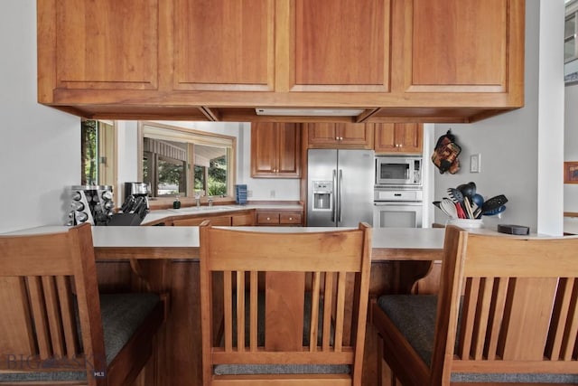 8A Gallatin Dr, Bozeman, MT 59718 - kitchen with stainless steel appliances, a breakfast bar, light countertops, brown cabinetry, and a peninsula