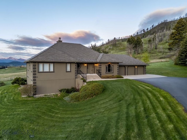 10423 Bridger Canyon Rd, Bozeman, MT 59715 - view of front of home featuring an attached garage, asphalt driveway, a mountain view, a yard, and stucco siding