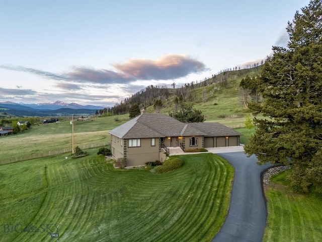 10423 Bridger Canyon Rd, Bozeman, MT 59715 - view of front of house with an attached garage, driveway, a mountain view, stucco siding, and a front lawn