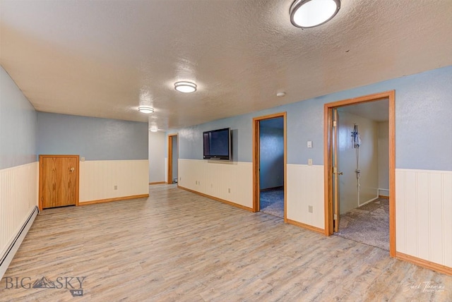 620 Higgins, Deer Lodge, MT 59722 - spare room with baseboard heating, a wainscoted wall, a textured ceiling, and light wood-style floors