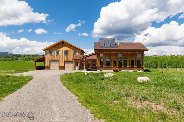 241 Aspen Loop Rd, West Yellowstone, MT 59758 - view of front of house with board and batten siding, gravel driveway, a garage, solar panels, and a front lawn
