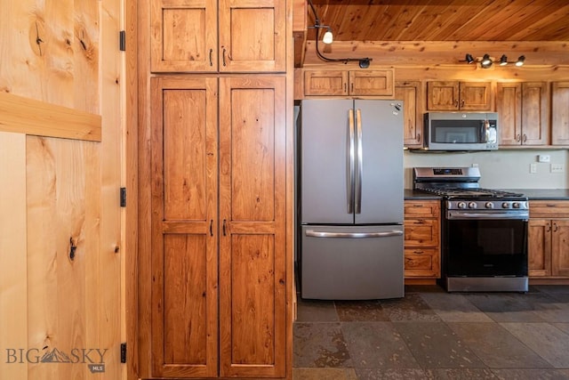241 Aspen Loop Rd, West Yellowstone, MT 59758 - kitchen with appliances with stainless steel finishes, wood ceiling, dark countertops, brown cabinetry, and dark stone finish flooring