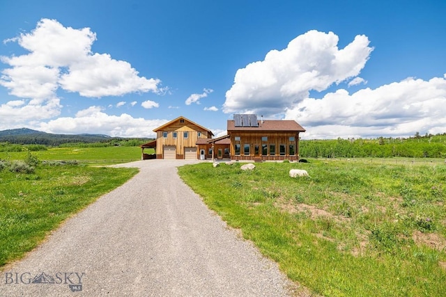 241 Aspen Loop Rd, West Yellowstone, MT 59758 - view of front of property featuring gravel driveway, an attached garage, roof mounted solar panels, and a view of rural / pastoral area