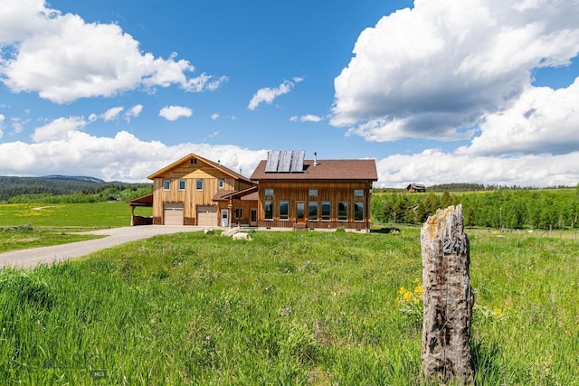 241 Aspen Loop Rd, West Yellowstone, MT 59758 - view of front facade featuring an attached garage, roof mounted solar panels, driveway, a rural view, and board and batten siding