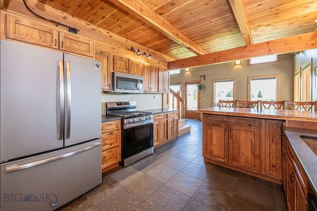 241 Aspen Loop Rd, West Yellowstone, MT 59758 - kitchen featuring appliances with stainless steel finishes, a wood ceiling with exposed beams, dark countertops, brown cabinetry, and stone tile floors