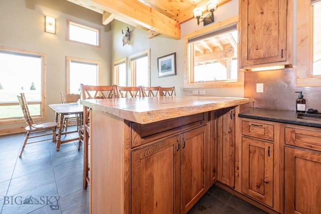241 Aspen Loop Rd, West Yellowstone, MT 59758 - kitchen with a breakfast bar, brown cabinets, dark tile patterned flooring, tasteful backsplash, and a wooden ceiling with exposed beams