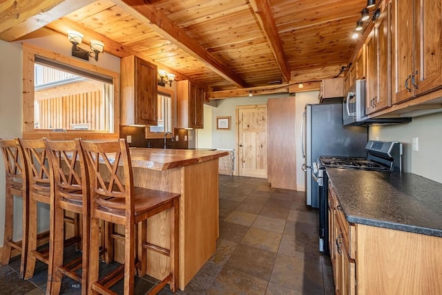 241 Aspen Loop Rd, West Yellowstone, MT 59758 - kitchen featuring range with gas cooktop, a wood ceiling with exposed beams, brown cabinetry, stainless steel microwave, and a kitchen bar