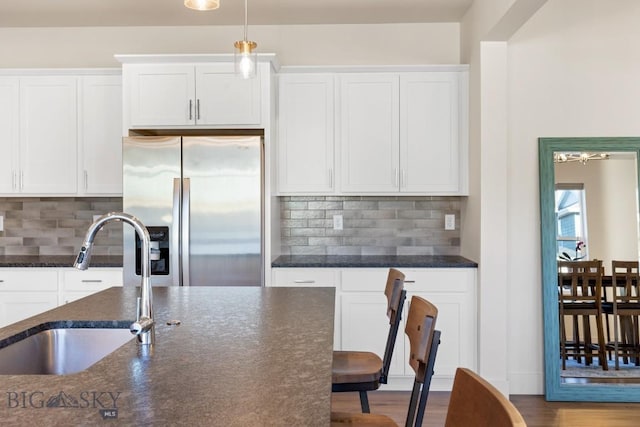 1606 Wyatt Earp Ct, Belgrade, MT 59714 - kitchen with stainless steel fridge, white cabinets, backsplash, dark stone counters, and wood finished floors