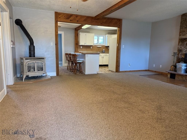 512 W 4th Ave, Big Timber, MT 59011 - unfurnished living room featuring a wood stove, beamed ceiling, and light colored carpet