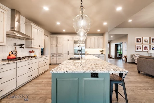 16 Tight Loop Dr, Bozeman, MT 59718 - kitchen featuring wall chimney range hood, stainless steel gas cooktop, backsplash, light wood finished floors, and a breakfast bar