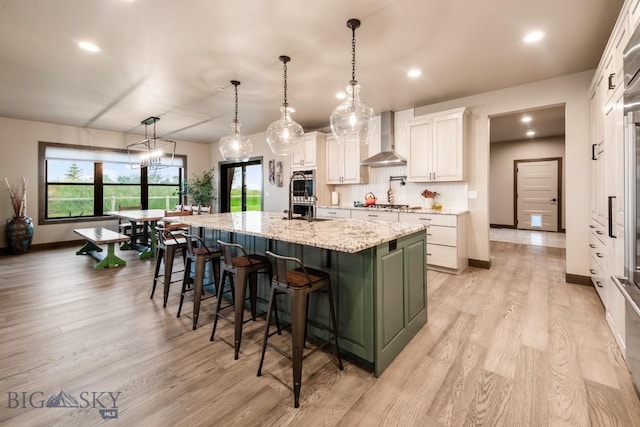16 Tight Loop Dr, Bozeman, MT 59718 - kitchen with wall chimney range hood, white cabinetry, light wood finished floors, a large island with sink, and a kitchen bar