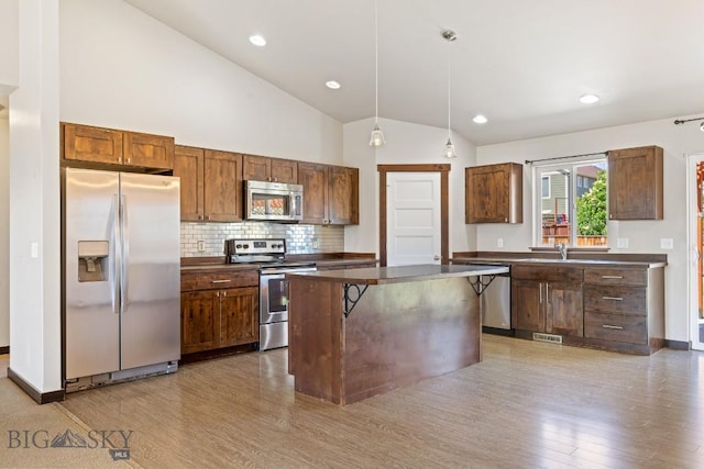 343 Stewart Loop, Bozeman, MT 59718 - kitchen featuring appliances with stainless steel finishes, dark countertops, wood finished floors, vaulted ceiling, and decorative backsplash