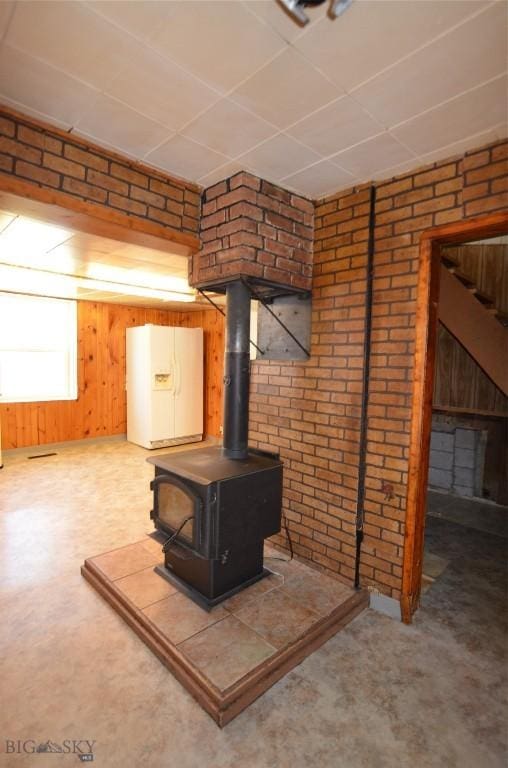 103 Flick, Sheridan, MT 59749 - basement featuring white refrigerator with ice dispenser, a wood stove, brick wall, and wooden walls