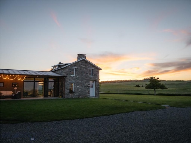 802 Deadmans Canyon Rd, Reed Point, MT 59069 - property exterior at dusk featuring stone siding, a chimney, a lawn, and a standing seam roof