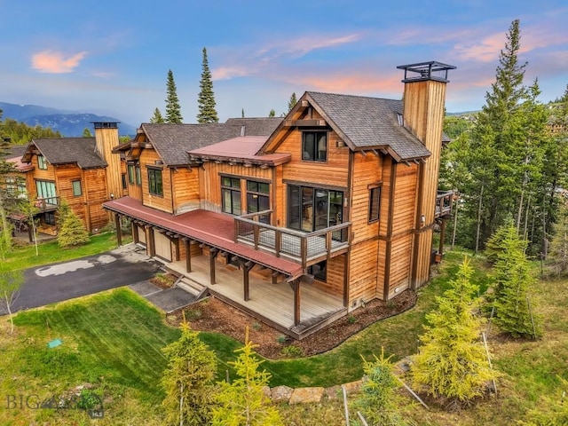 146 Outlook Trl, Big Sky, MT 59716 - rear view of house featuring a chimney, a garage, asphalt driveway, a wooden deck, and a yard