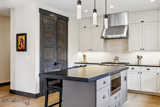 146 Outlook Trl, Big Sky, MT 59716 - kitchen with wall chimney range hood, light wood-type flooring, dark countertops, appliances with stainless steel finishes, and a kitchen island