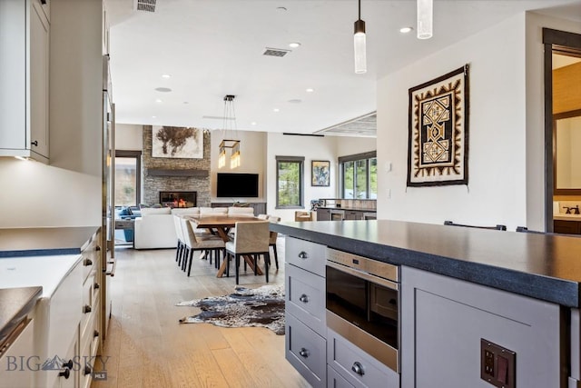 146 Outlook Trl, Big Sky, MT 59716 - kitchen with light wood finished floors, dark countertops, a stone fireplace, hanging light fixtures, and gray cabinetry