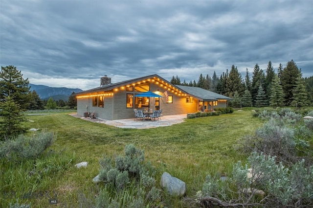 17 Chief Joseph Trl, Big Sky, MT 59716 - rear view of house featuring a chimney, a patio area, a lawn, and a mountain view