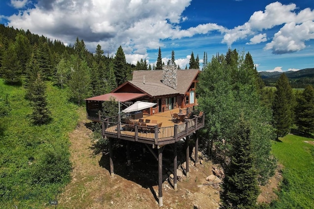 11540 Taiga Trl, Bozeman, MT 59715 - back of property featuring a wooden deck, outdoor dining area, a chimney, and a forest view