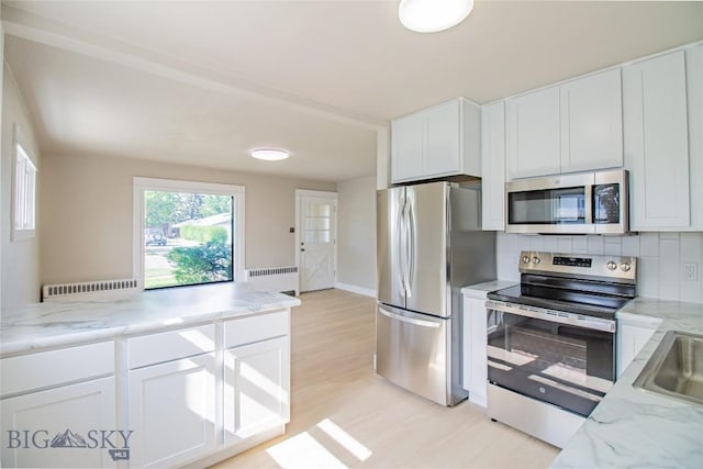 1940 Locust, Butte, MT 59701 - kitchen with appliances with stainless steel finishes, radiator, white cabinetry, light stone countertops, and decorative backsplash