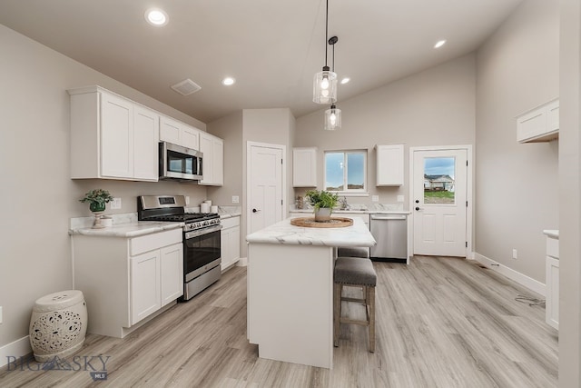 2204 Oriole Dr, Belgrade, MT 59714 - kitchen with stainless steel appliances, white cabinets, light wood-style floors, a breakfast bar, and high vaulted ceiling