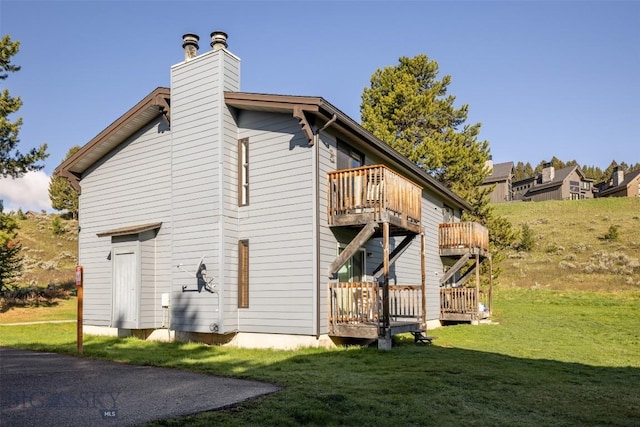 139 Spruce Cone Dr Unit 14, Big Sky, MT 59716 - back of property featuring a balcony, a lawn, a chimney, and a deck