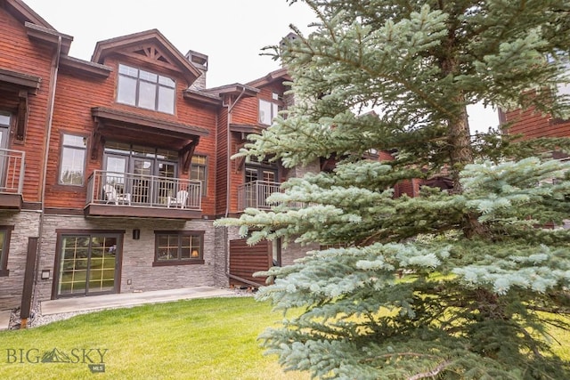 2500 Little Coyote Rd Unit 34, Big Sky, MT 59716 - rear view of property featuring a chimney, a balcony, stone siding, and a yard