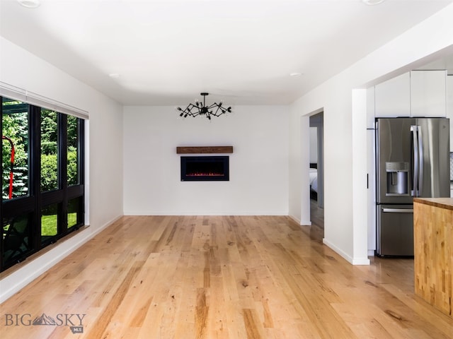 1206 N Cedarview Dr, Bozeman, MT 59715 - unfurnished living room with light wood-type flooring, a warm lit fireplace, and a chandelier