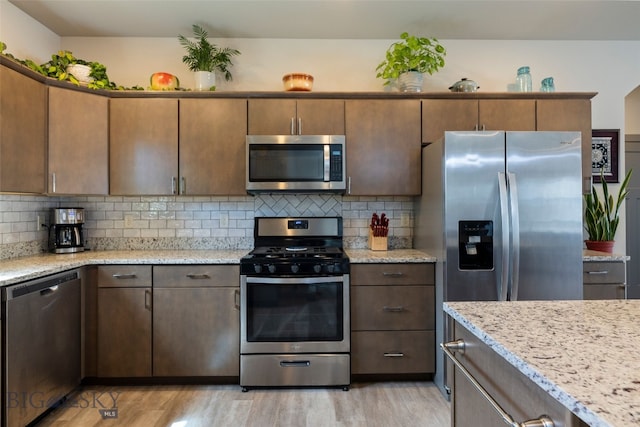 1308 Scooter Ln, Belgrade, MT 59714 - kitchen with stainless steel appliances, light wood-type flooring, decorative backsplash, and light stone counters