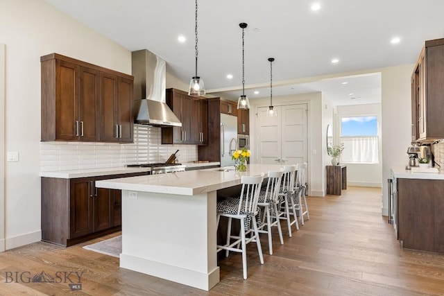 20 Caymus Ln Unit D, Bozeman, MT 59718 - kitchen featuring wall chimney exhaust hood, a kitchen island with sink, tasteful backsplash, high end refrigerator, and light wood finished floors