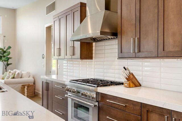 20 Caymus Ln Unit D, Bozeman, MT 59718 - kitchen with wall chimney exhaust hood, high end range, backsplash, and dark brown cabinets
