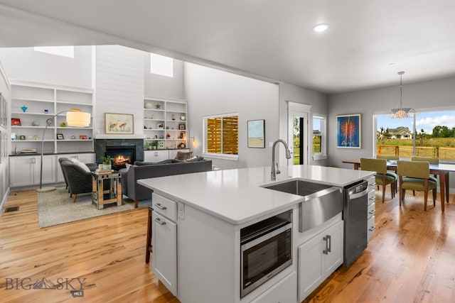 85 Riparian Way, Bozeman, MT 59718 - kitchen featuring stainless steel appliances, a warm lit fireplace, an island with sink, light wood finished floors, and decorative light fixtures
