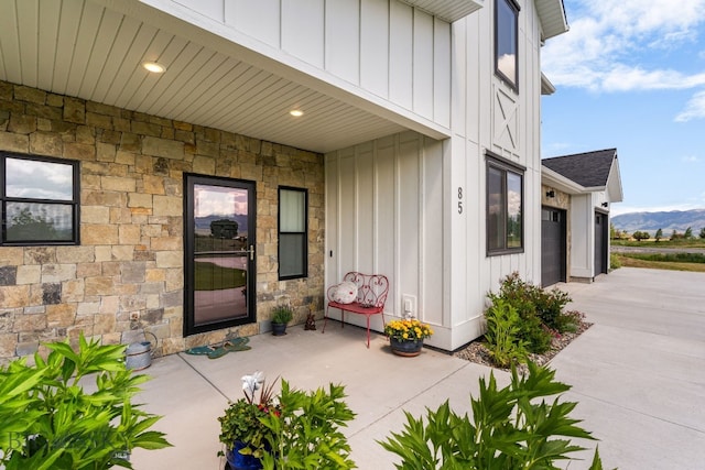85 Riparian Way, Bozeman, MT 59718 - entrance to property with board and batten siding, stone siding, concrete driveway, a shingled roof, and a mountain view
