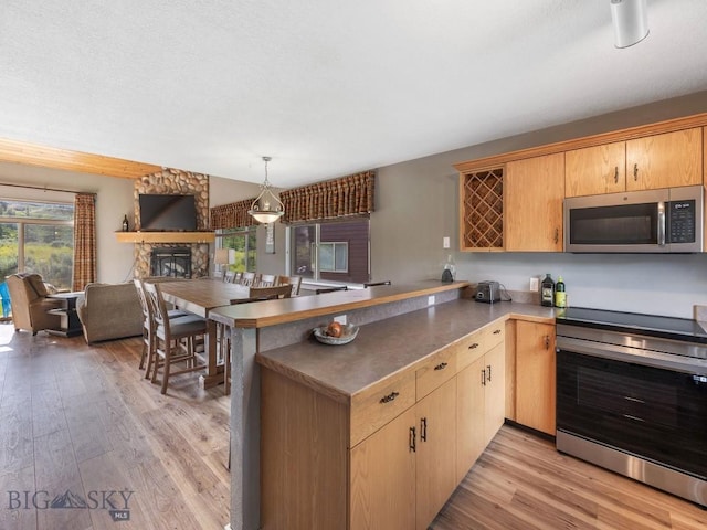 417 Firelight, Big Sky, MT 59716 - kitchen featuring stainless steel appliances, a peninsula, light wood-style floors, and a fireplace