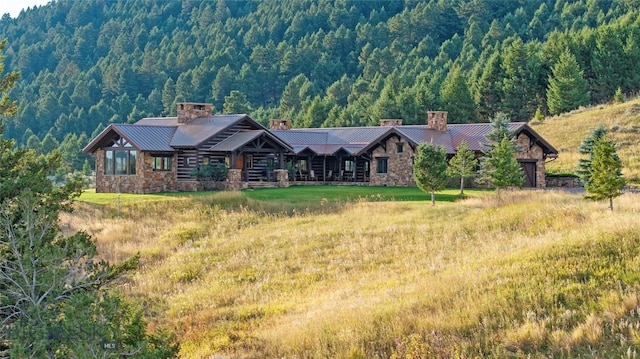 94 Sky Band Trl, Livingston, MT 59047 - view of front facade featuring a chimney, stone siding, a view of trees, and a standing seam roof