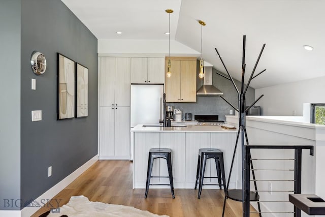 1492 Windrow Dr, Bozeman, MT 59718 - kitchen featuring wall chimney range hood, light countertops, a breakfast bar, light wood-type flooring, and high quality fridge