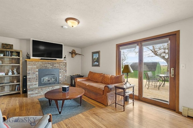 109 Cottonwood St, Manhattan, MT 59741 - living room featuring light wood-style flooring, a textured ceiling, a brick fireplace, and baseboard heating