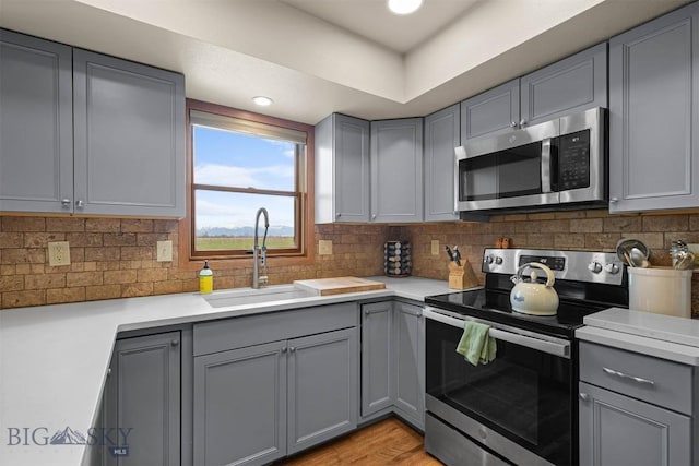 109 Cottonwood St, Manhattan, MT 59741 - kitchen featuring stainless steel appliances, gray cabinets, light countertops, backsplash, and light wood-style flooring