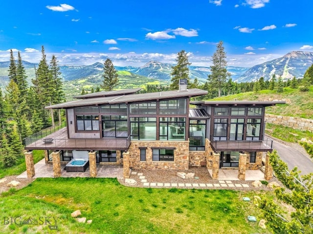 93 Goshawk Trl, Big Sky, MT 59716 - back of property featuring a patio area, a sunroom, a hot tub, and a mountain view