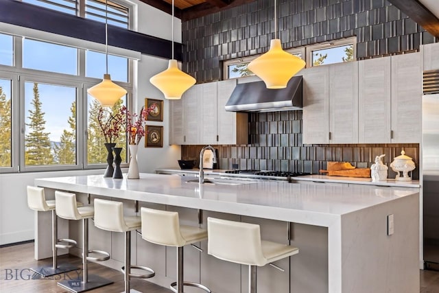 93 Goshawk Trl, Big Sky, MT 59716 - kitchen featuring wall chimney exhaust hood, tasteful backsplash, an island with sink, wood finished floors, and light countertops