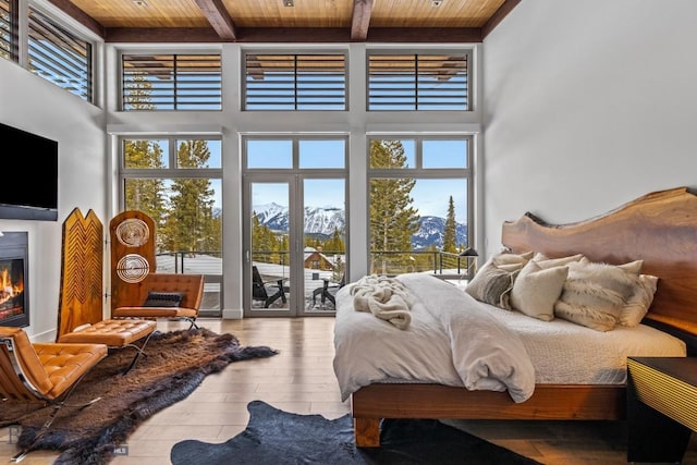 93 Goshawk Trl, Big Sky, MT 59716 - bedroom with a wooden ceiling with exposed beams, a mountain view, a towering ceiling, multiple windows, and a glass covered fireplace