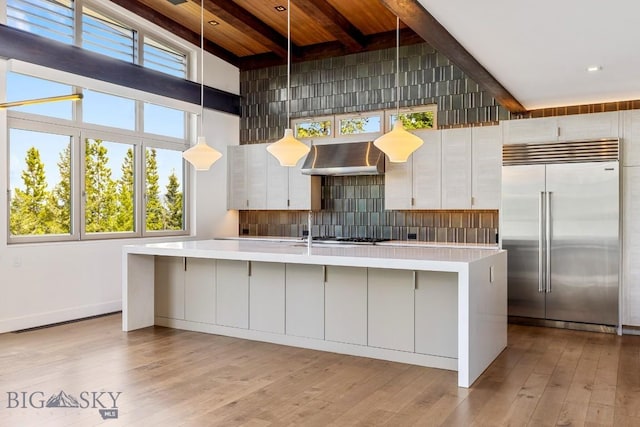 93 Goshawk Trl, Big Sky, MT 59716 - kitchen featuring stainless steel built in refrigerator, extractor fan, light countertops, light wood-style flooring, and a center island with sink