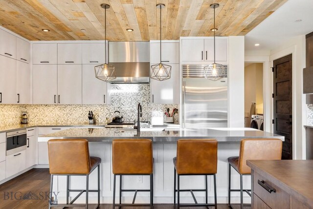 425 Outlook Trl, Big Sky, MT 59716 - kitchen with stainless steel built in fridge, wood ceiling, recessed lighting, hanging light fixtures, and wall chimney exhaust hood