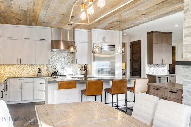 425 Outlook Trl, Big Sky, MT 59716 - kitchen featuring wall chimney exhaust hood, built in fridge, dark wood-style flooring, a kitchen island with sink, and modern cabinets