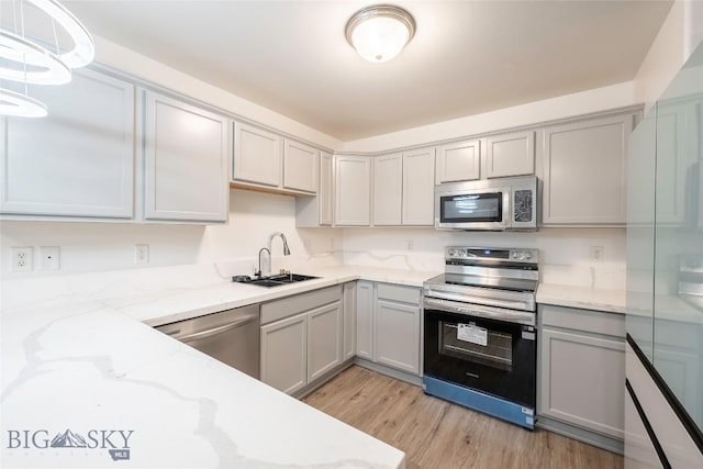 1010 Cruiser Ln Unit M, Belgrade, MT 59714 - kitchen featuring appliances with stainless steel finishes, gray cabinetry, light wood finished floors, and light stone counters