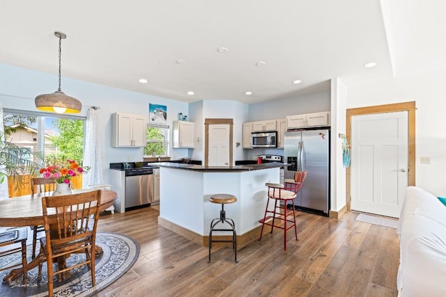 182 Snowy Owl Trl, Bozeman, MT 59718 - kitchen with appliances with stainless steel finishes, a center island, dark countertops, wood finished floors, and a breakfast bar
